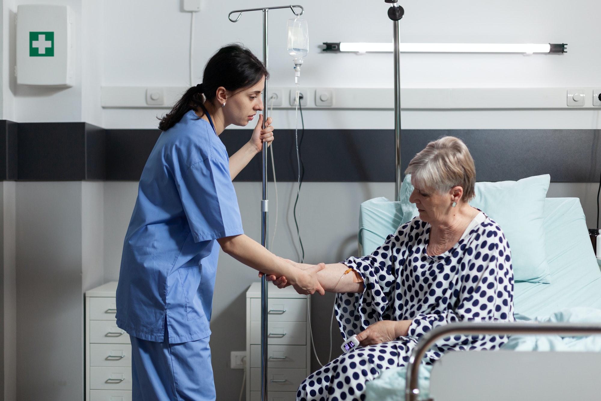 Medical nurse helping senior woman patient getting up from bed